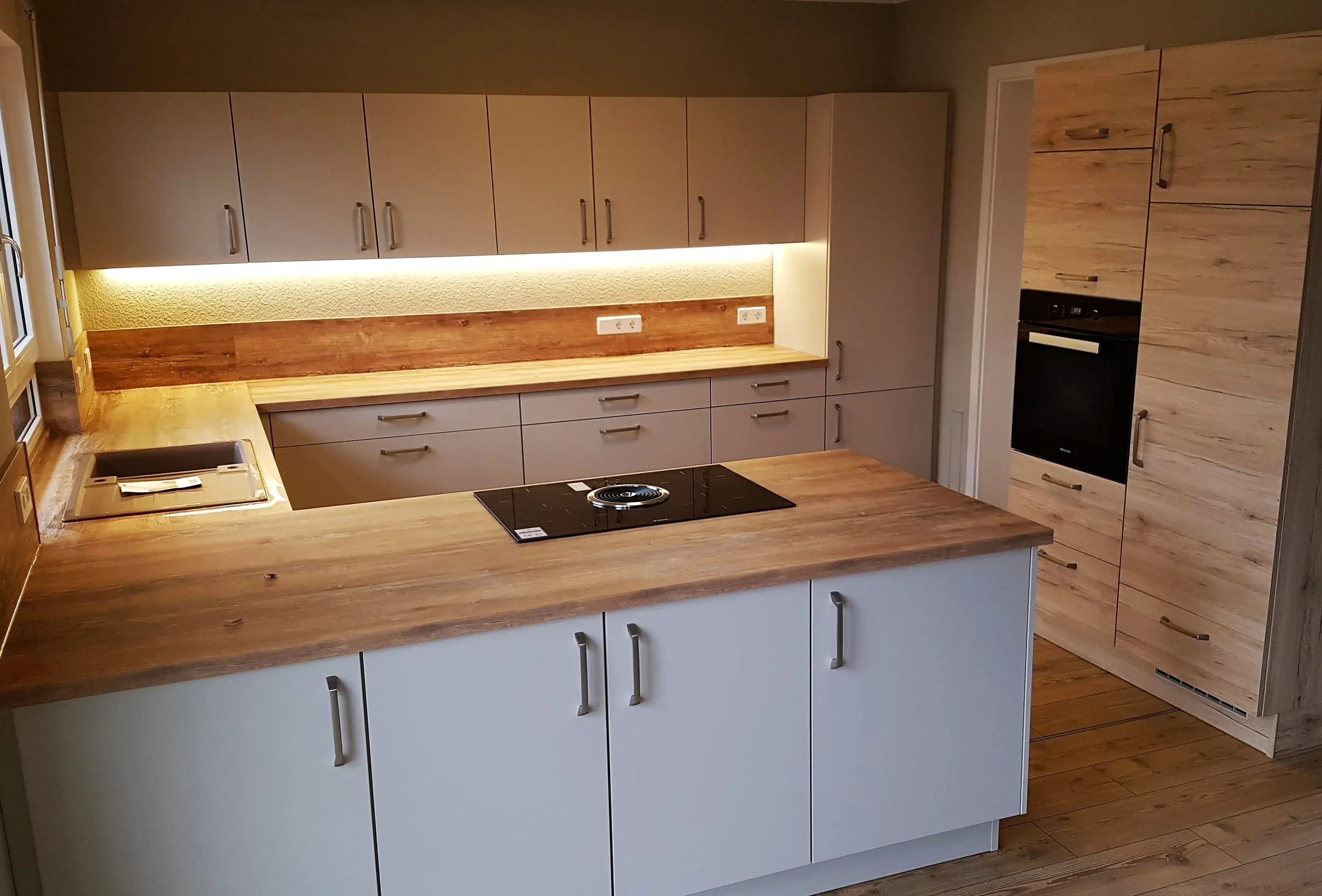 Moderne Einbauküche mit Holzarbeitsplatten und heller LED-Beleuchtung.