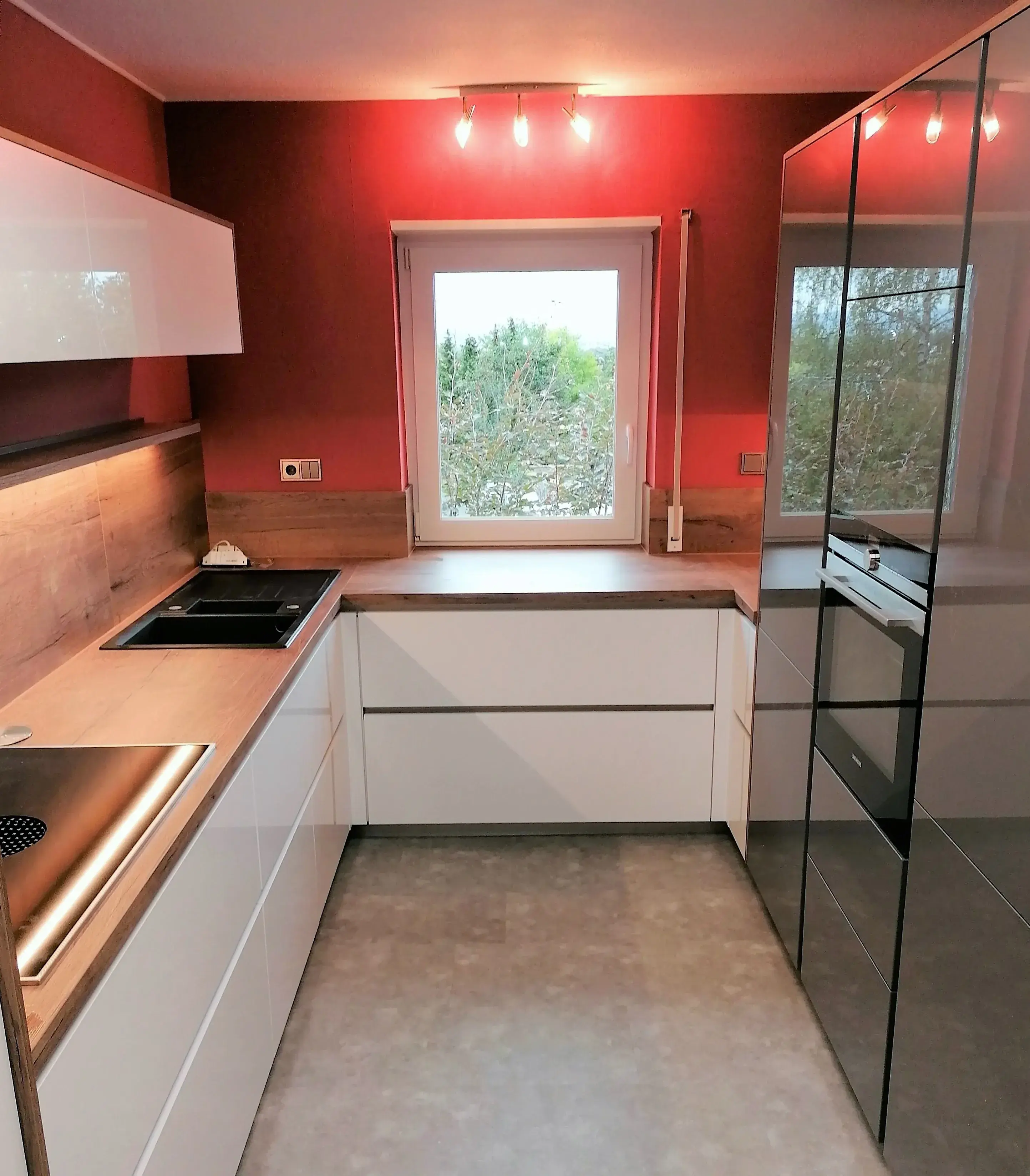 Moderne Küche mit weißen Schränken, Holzarbeitsplatte und roter Wand, Fenster mittig