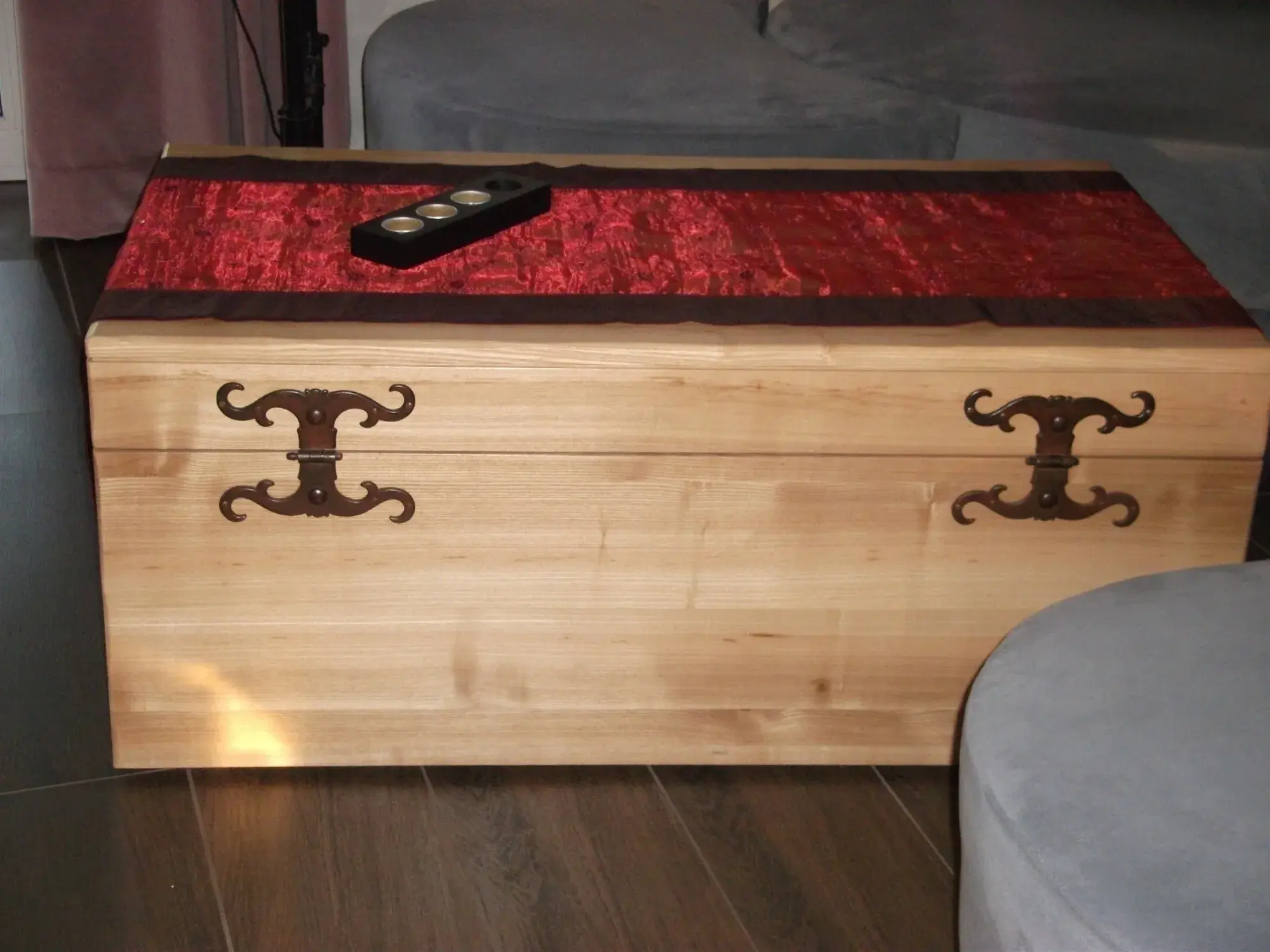 Holztruhe mit Metallbeschlägen, rote Decke und Fernbedienung darauf.