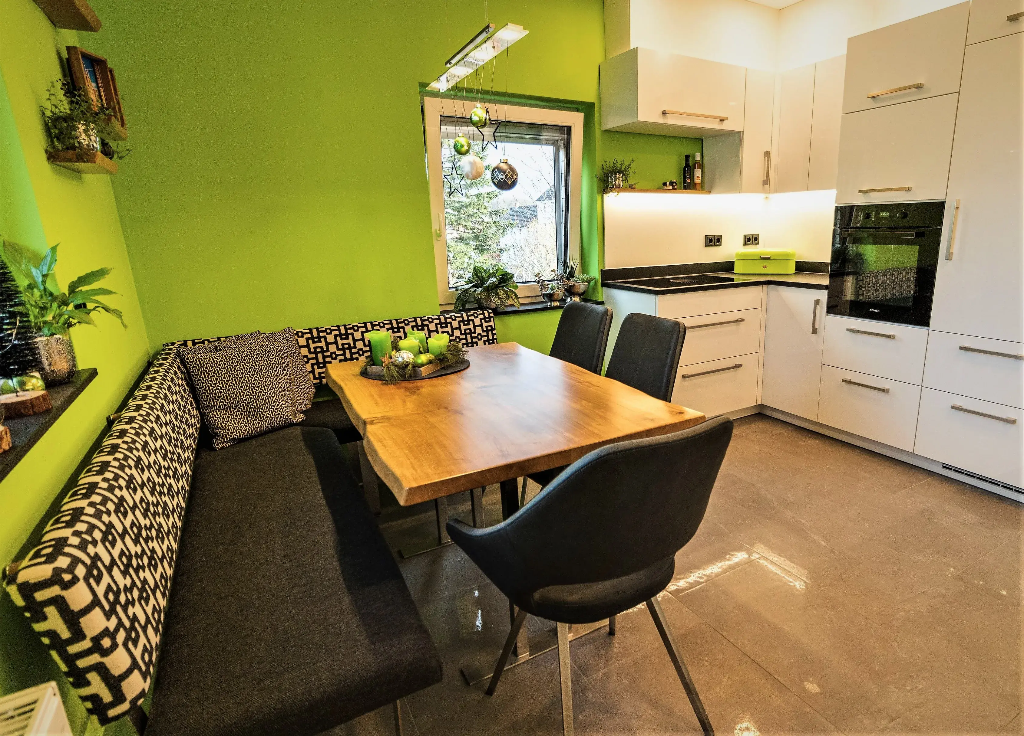 Moderne Küche mit grüner Wand, Eckbank, Holztisch und weißen Schränken.