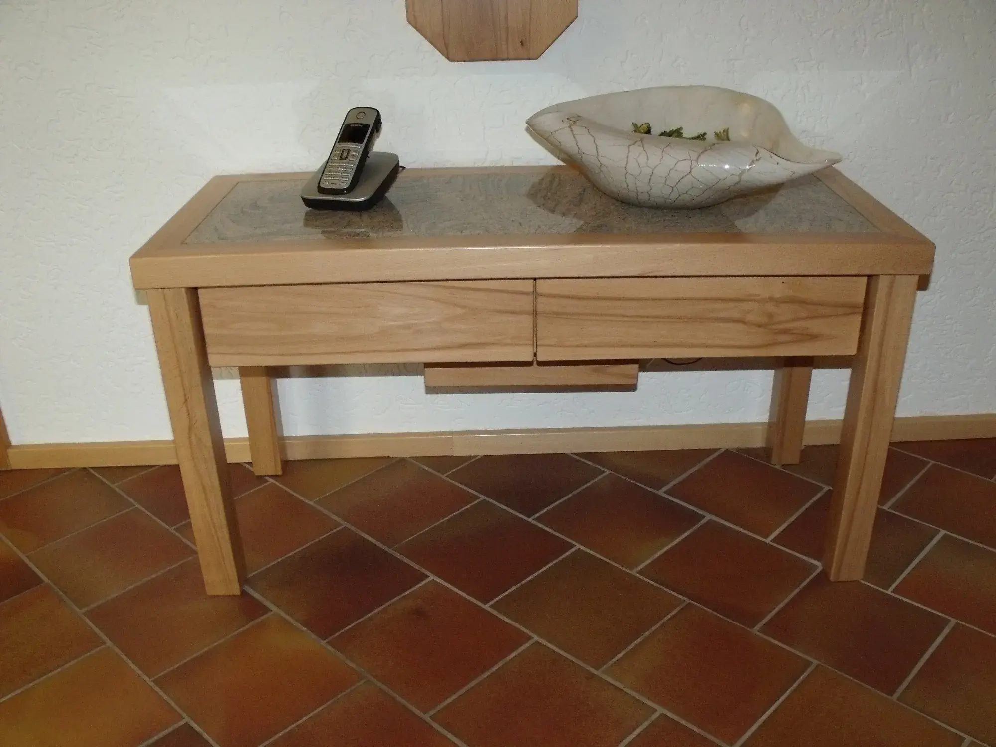 Holztisch mit zwei Schubladen, darauf eine Schale und ein Festnetztelefon.