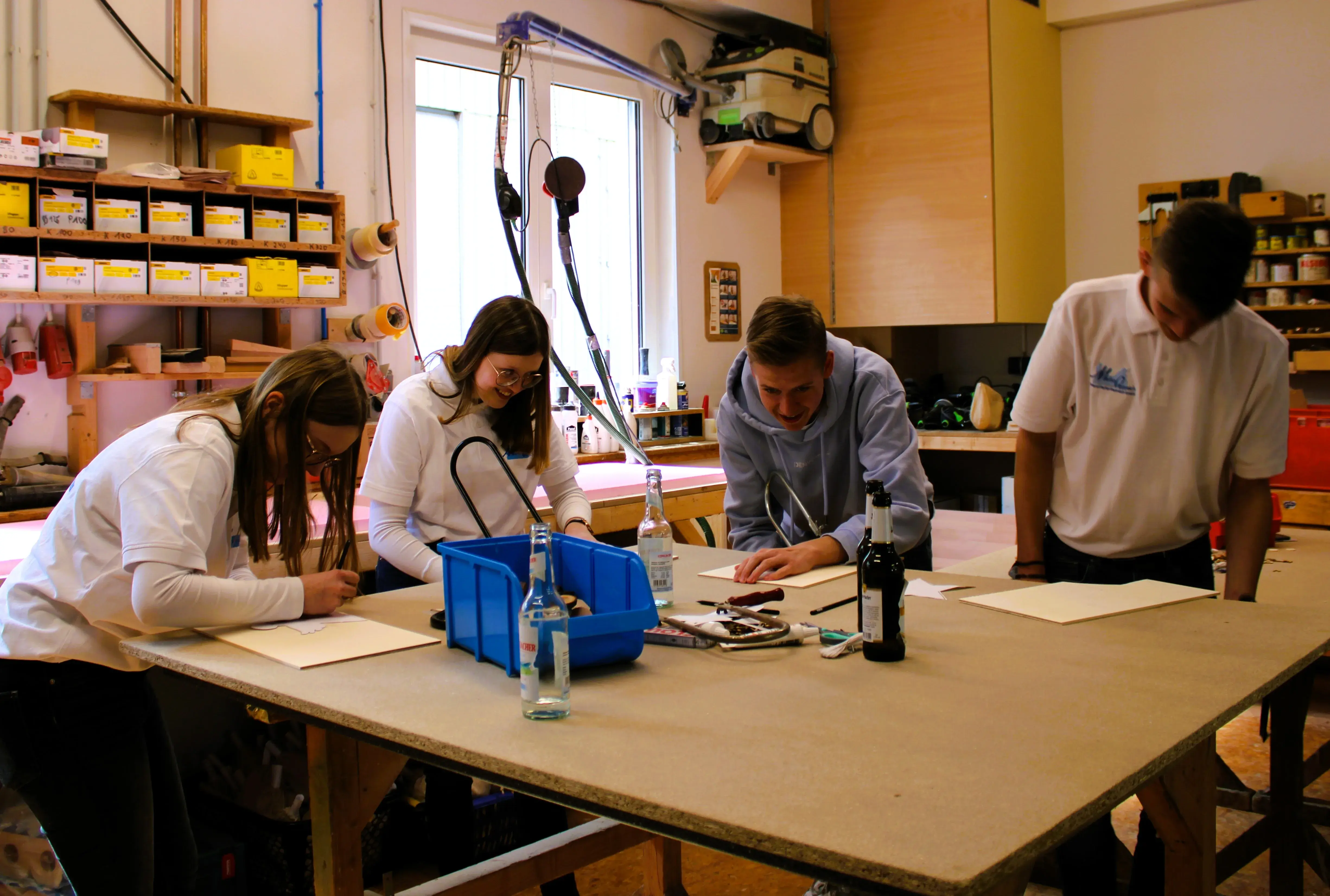Vier Jugendliche arbeiten konzentriert an einem großen Holztisch in einer Werkstatt.