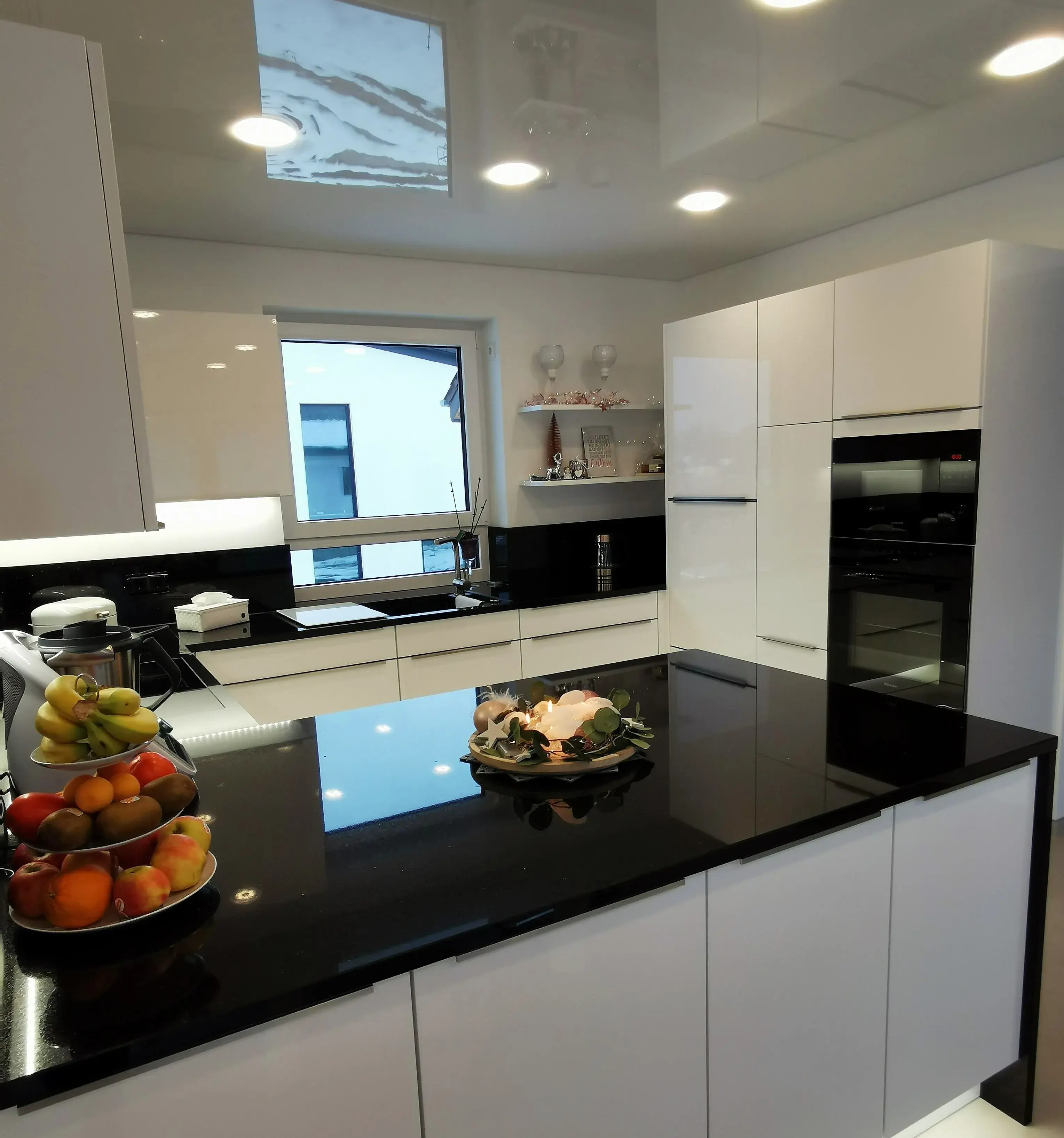 Moderne weiße Küche mit schwarzer Arbeitsplatte und Obstschale auf der Kochinsel.