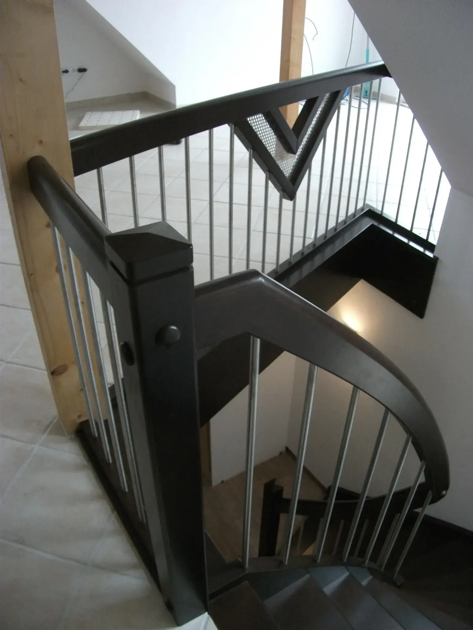 Moderne Treppe mit dunklem Geländer und Holzpfosten in einem hellen Treppenhaus.