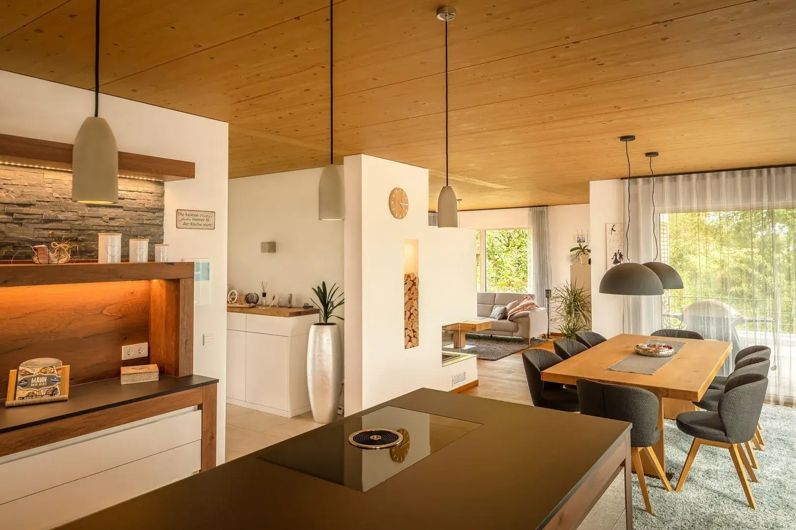 Moderne, helle Wohnküche mit Esstisch, Sofa und großen Fenstern zum Garten.