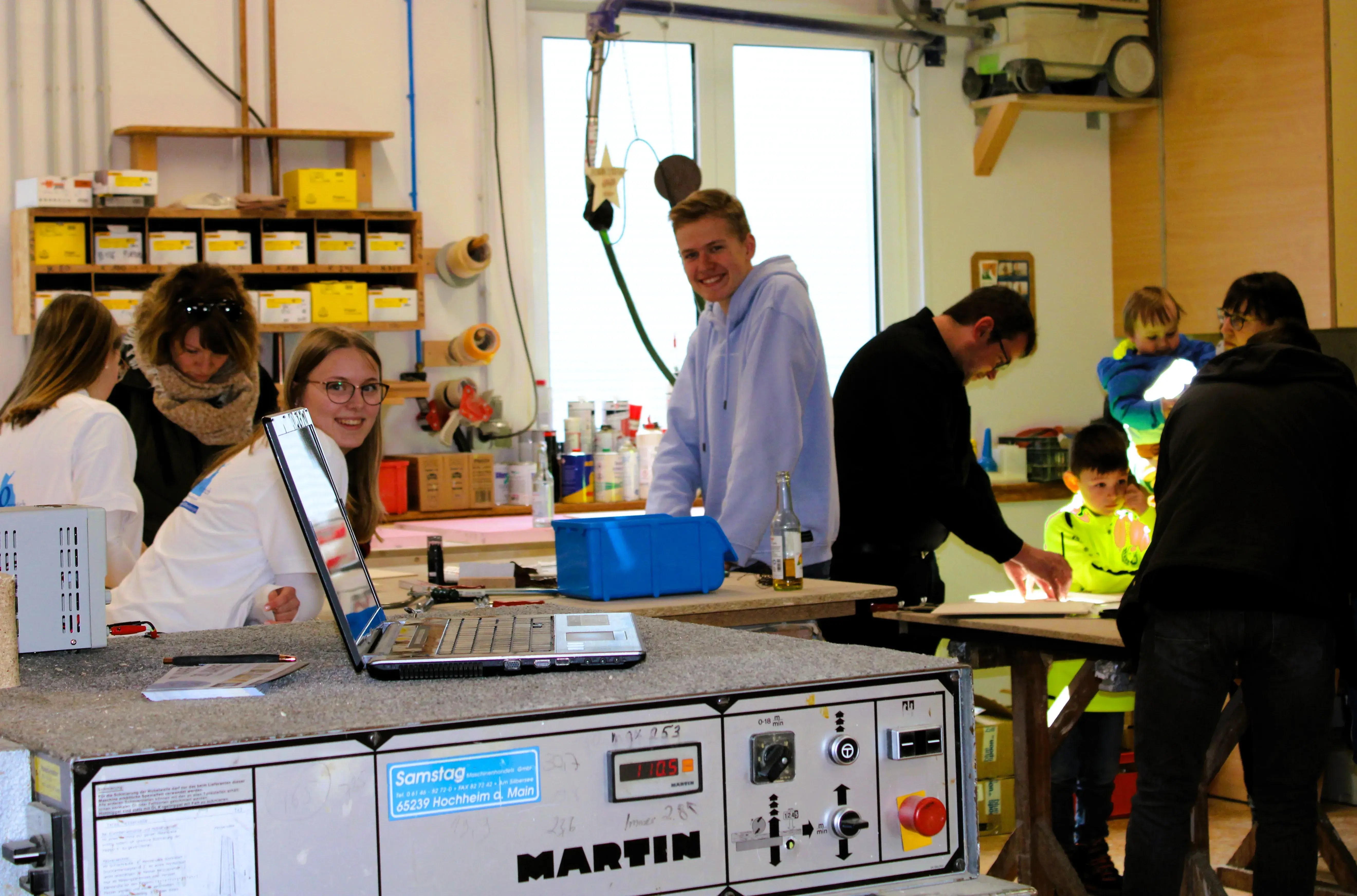 Menschen arbeiten gemeinsam in einer hellen Werkstatt mit Maschinen und Werkzeugen.