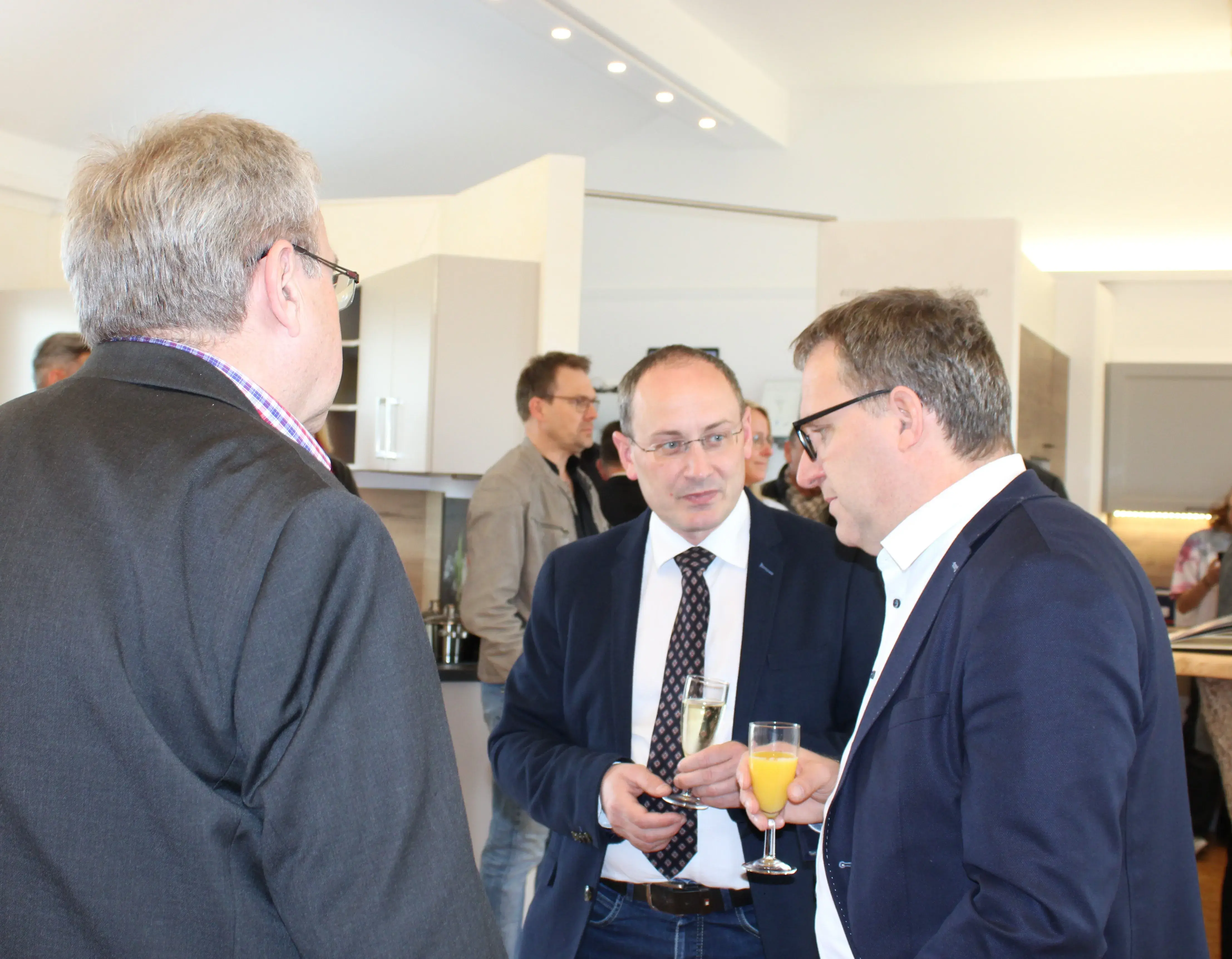 Drei Männer im Anzug unterhalten sich bei einem Empfang mit Getränken.