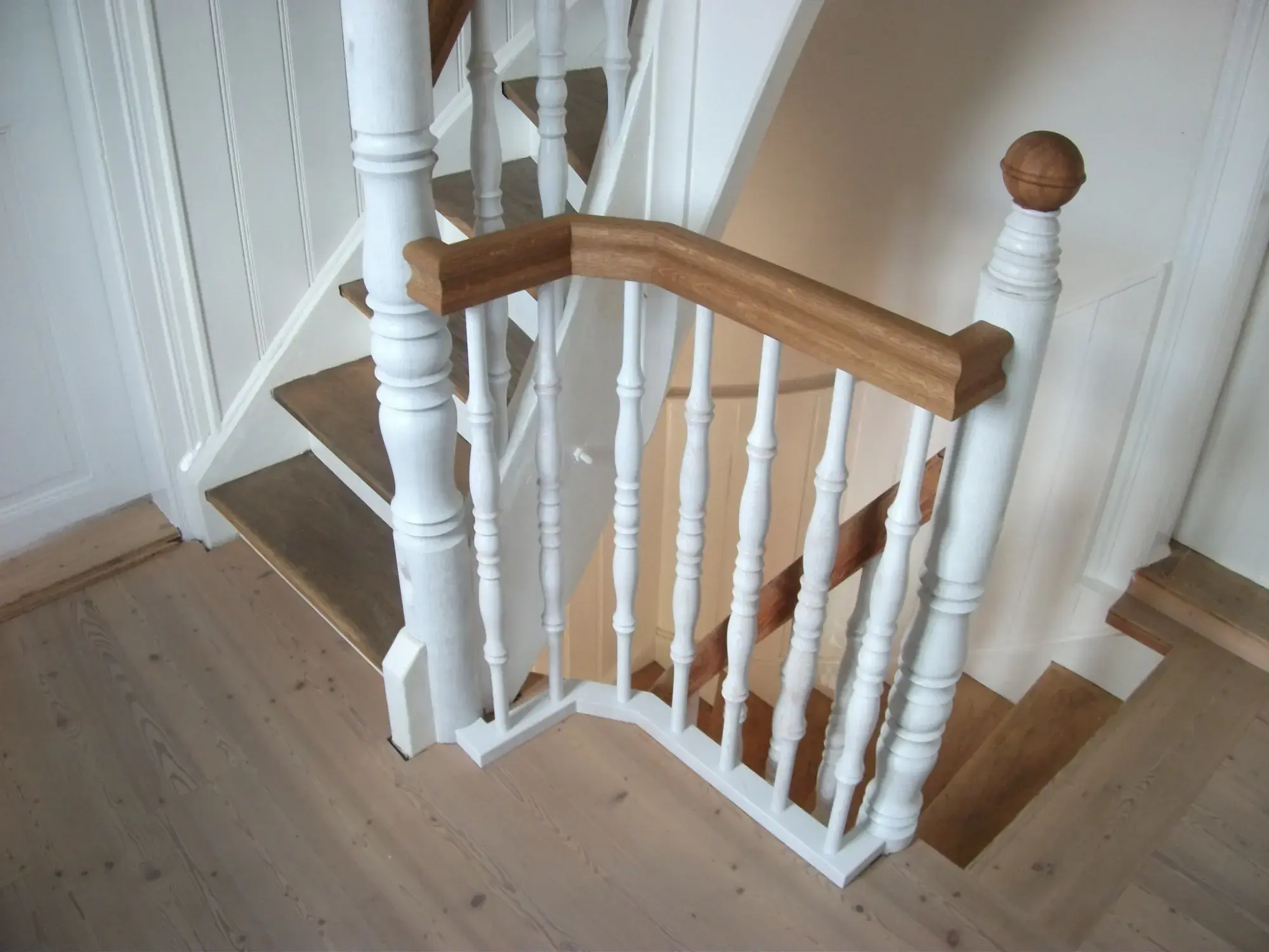 Weiße Holztreppe mit braunem Handlauf und hellen Stufen in einem Innenraum.