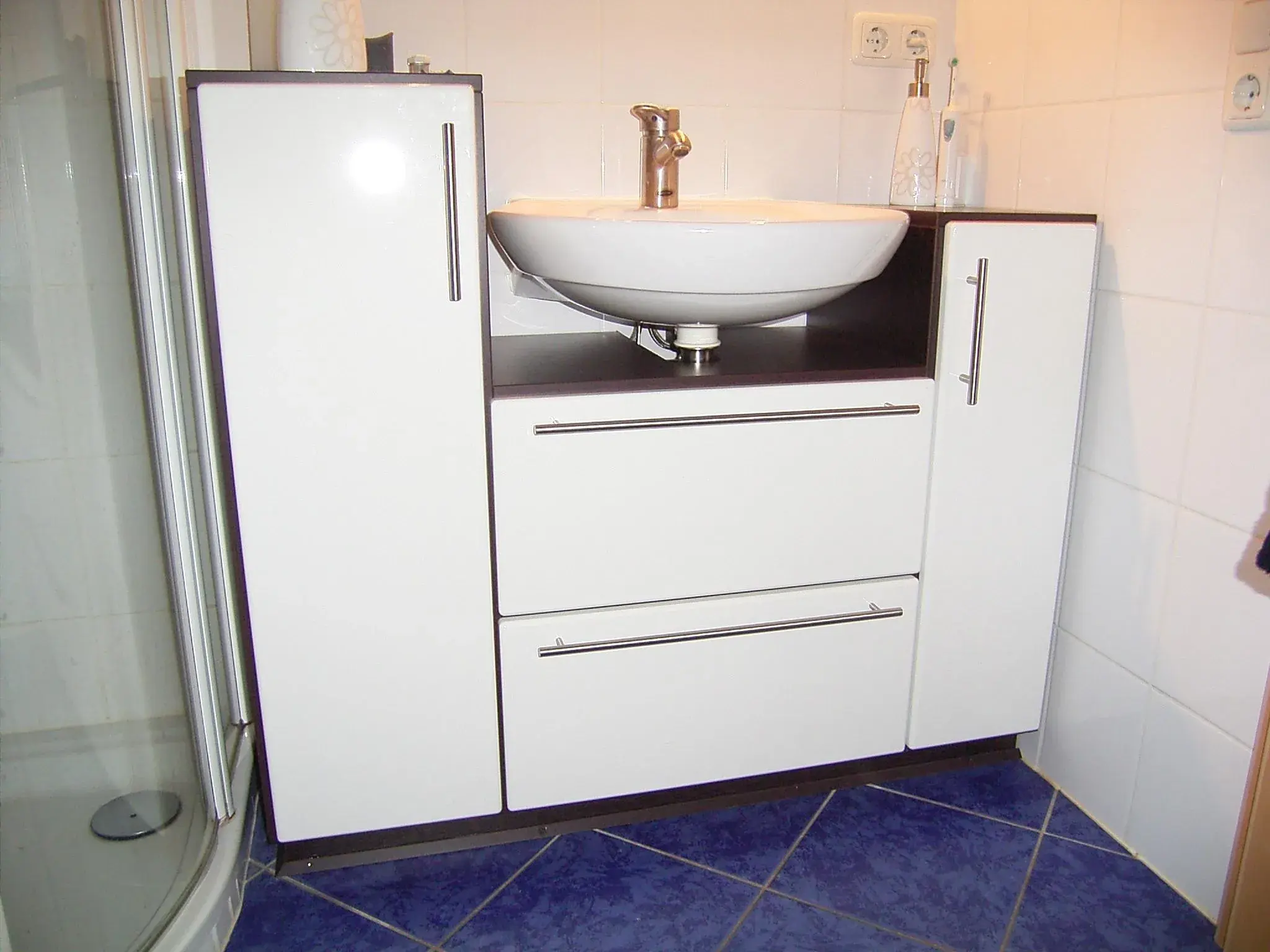 Waschtisch mit weißem Unterschrank, blauer Fliesenboden, Dusche links