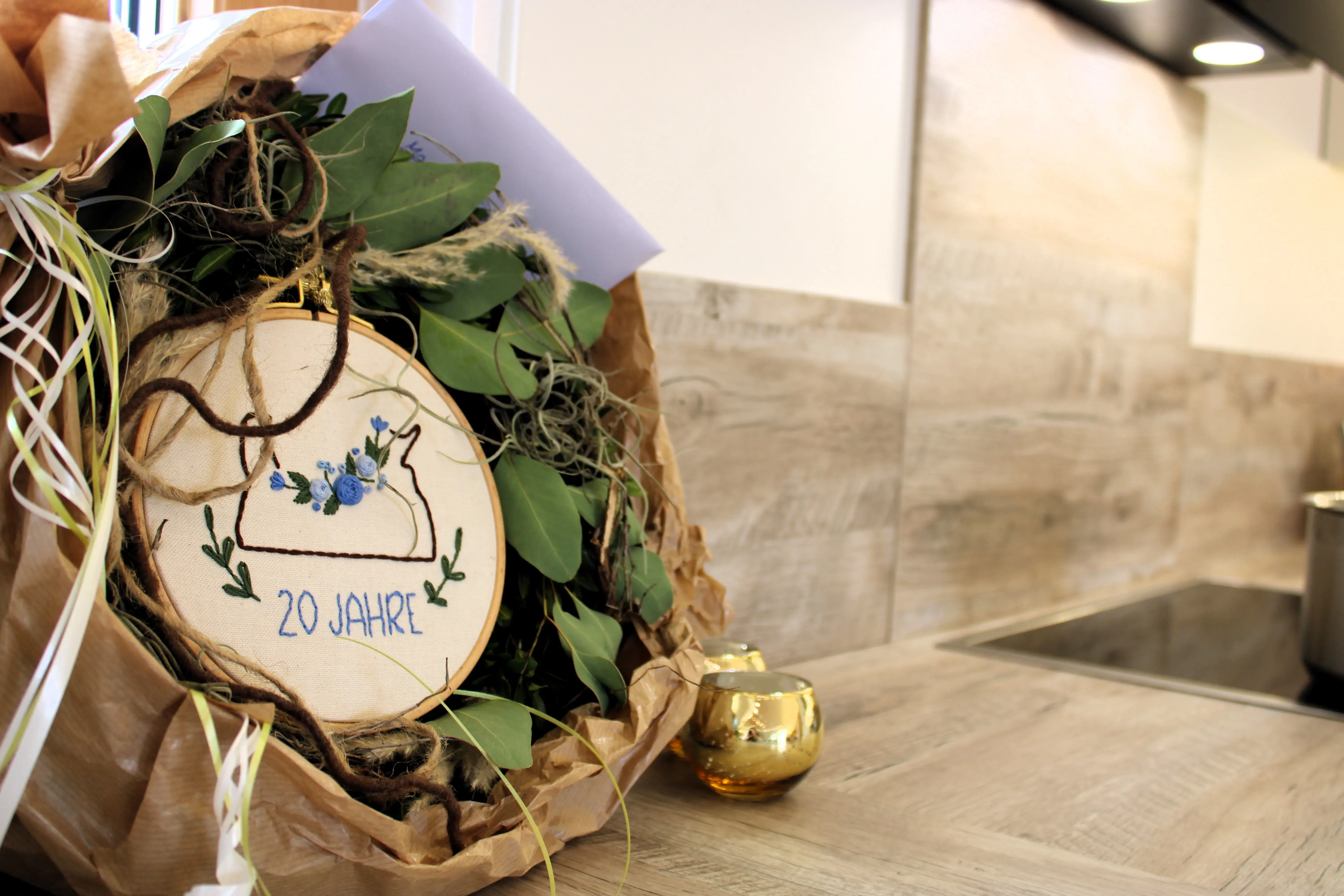 Blumenstrauß mit besticktem Holzschild „20 Jahre“ auf Küchentheke.