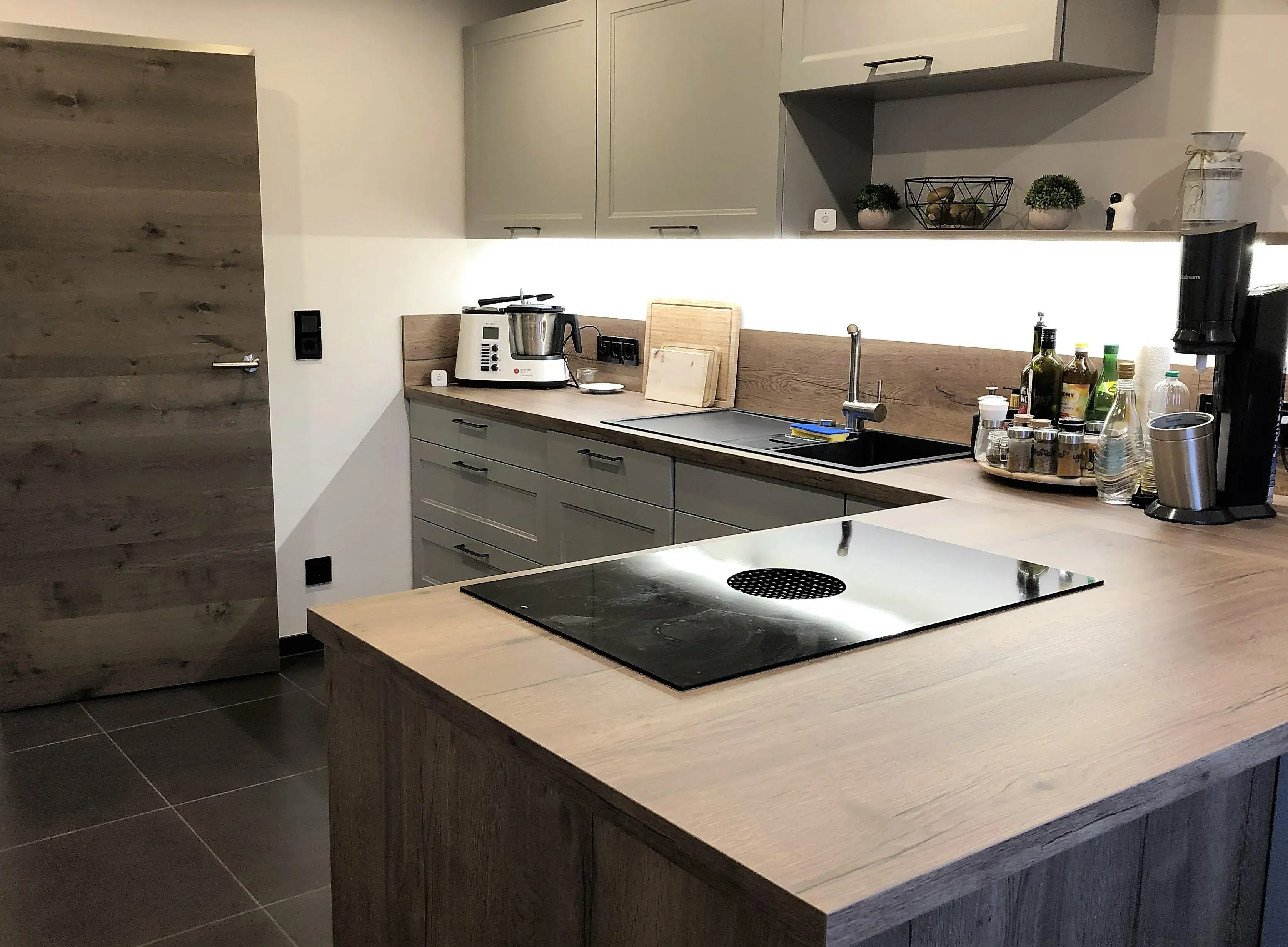 Moderne Küche mit Holzfronten, Kochfeld auf der Insel, Küchenutensilien und Beleuchtung.