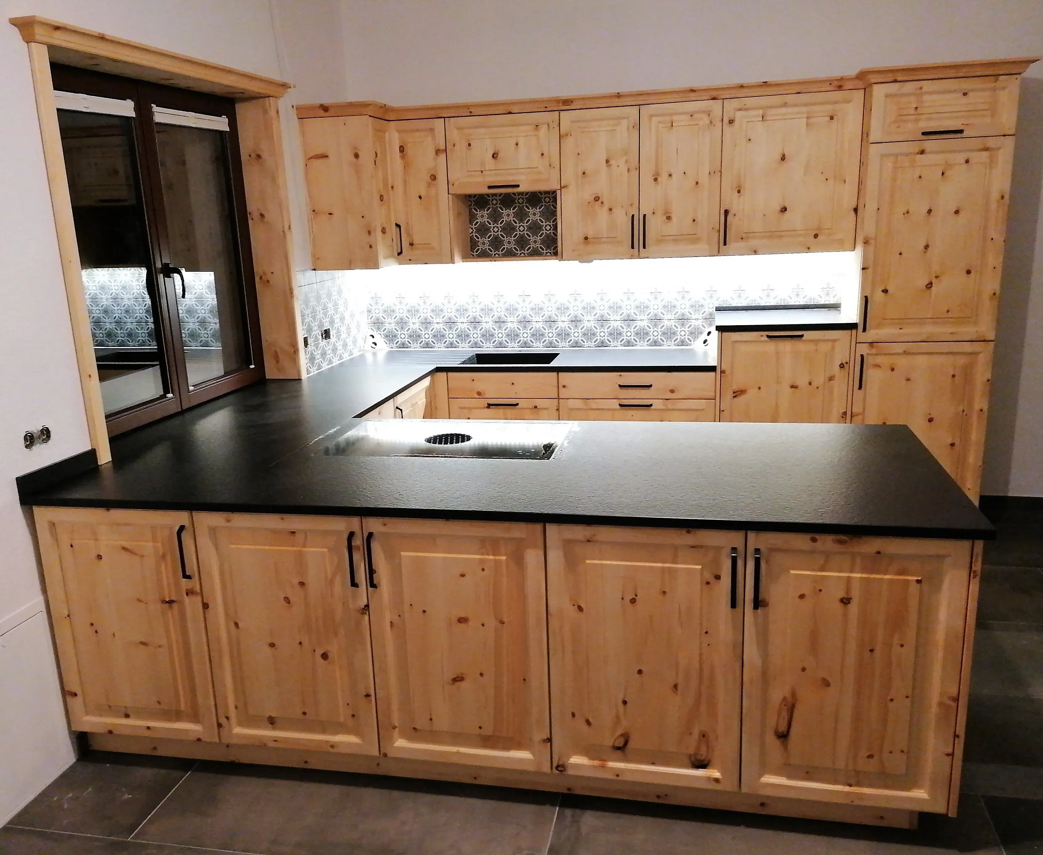 Küche mit hellen Holzschränken, schwarzer Arbeitsplatte und Fliesenrückwand.