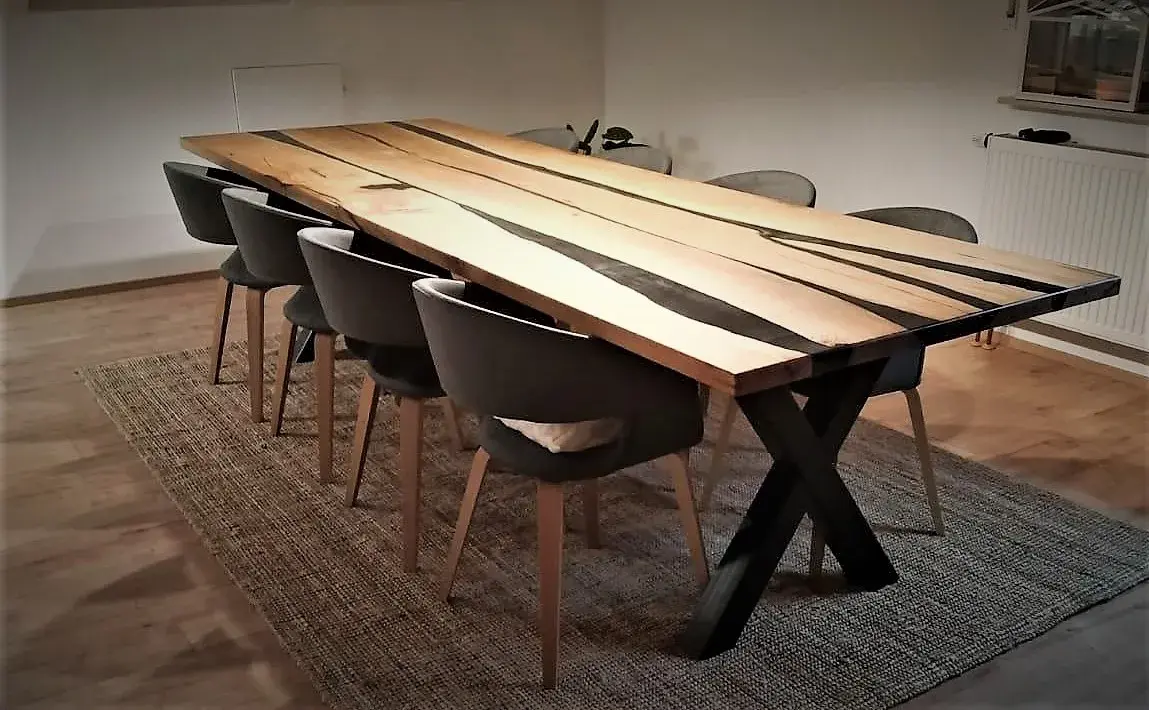 Langer Holztisch mit schwarzem Gestell und sechs grauen Stühlen auf einem Teppich.