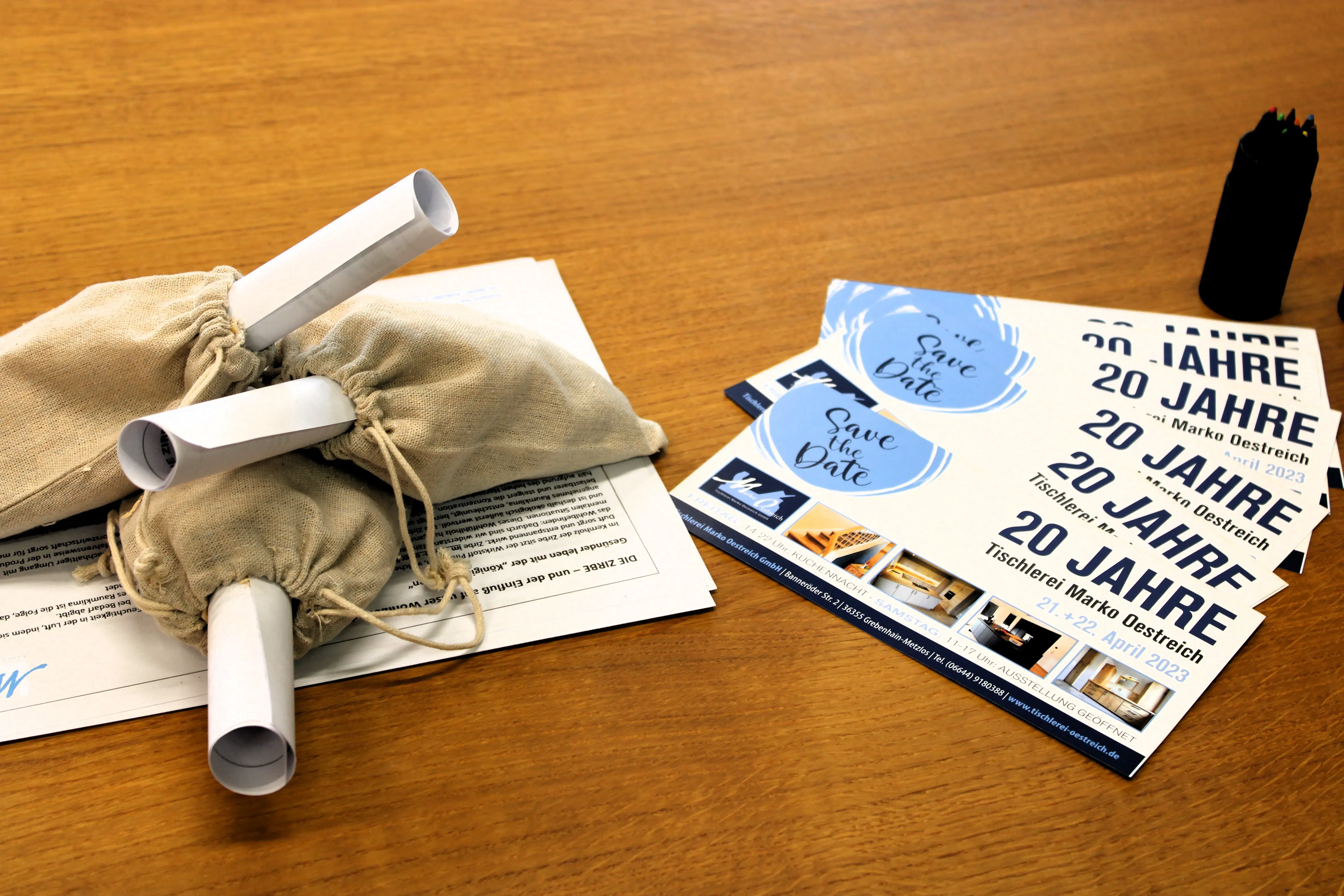 Stoffbeutel mit gerolltem Papier, daneben Flyer auf einem Holztisch.