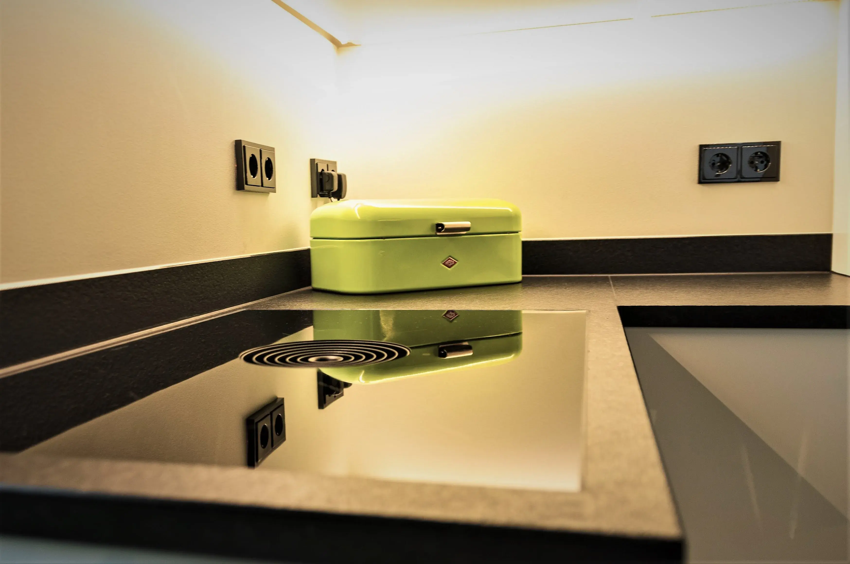 Moderne Küchenzeile mit Herdplatte und grüner Brotdose in der Ecke.