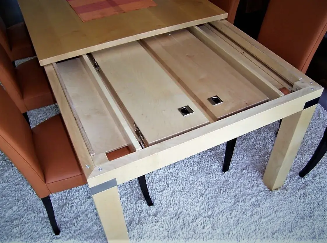 Ausziehbarer Holztisch mit ausgebauter Tischplatte, umgeben von braunen Stühlen.