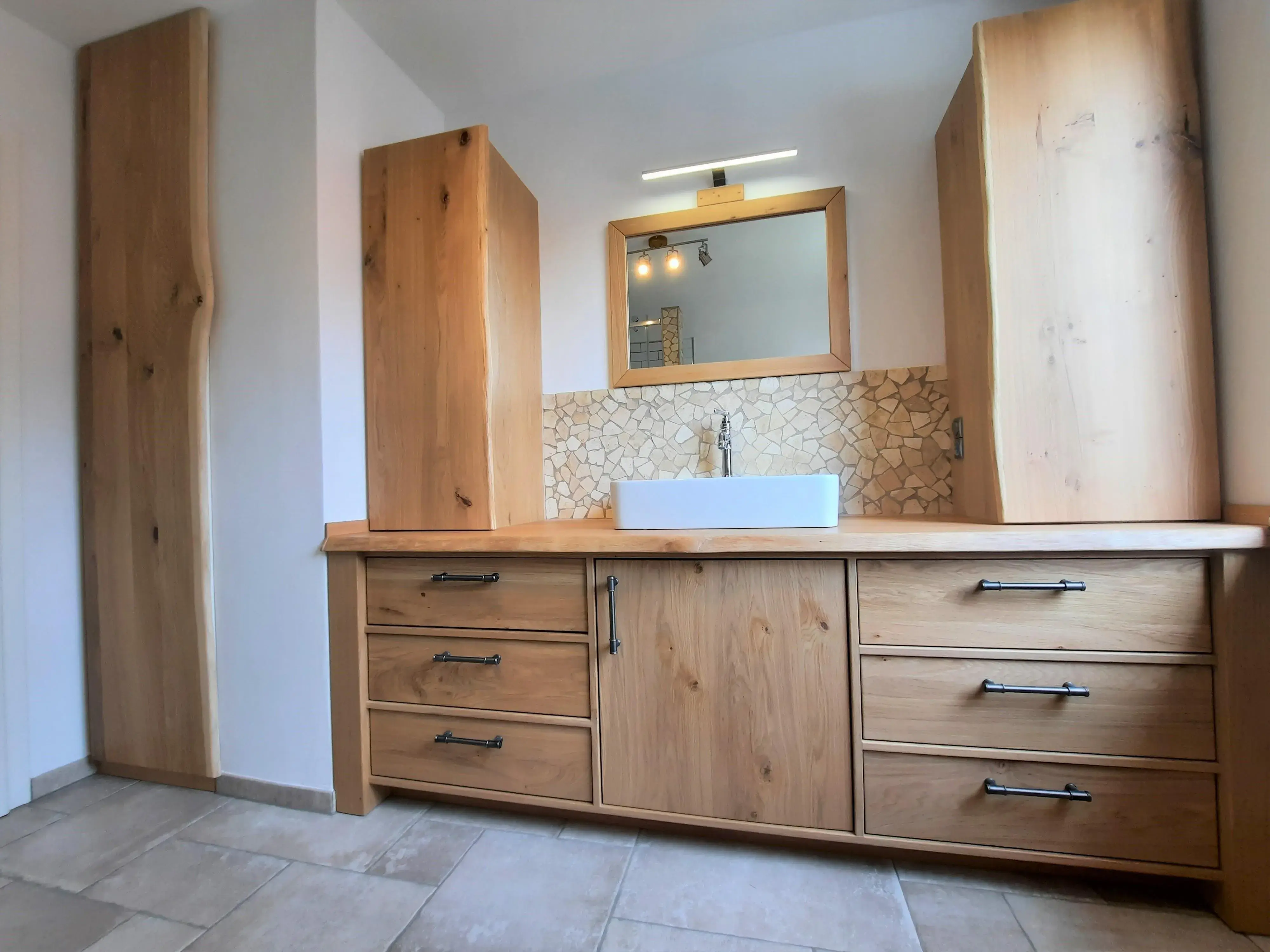 Waschbecken mit Holzunterschrank und Mosaikfliesen, beleuchteter Spiegel darüber