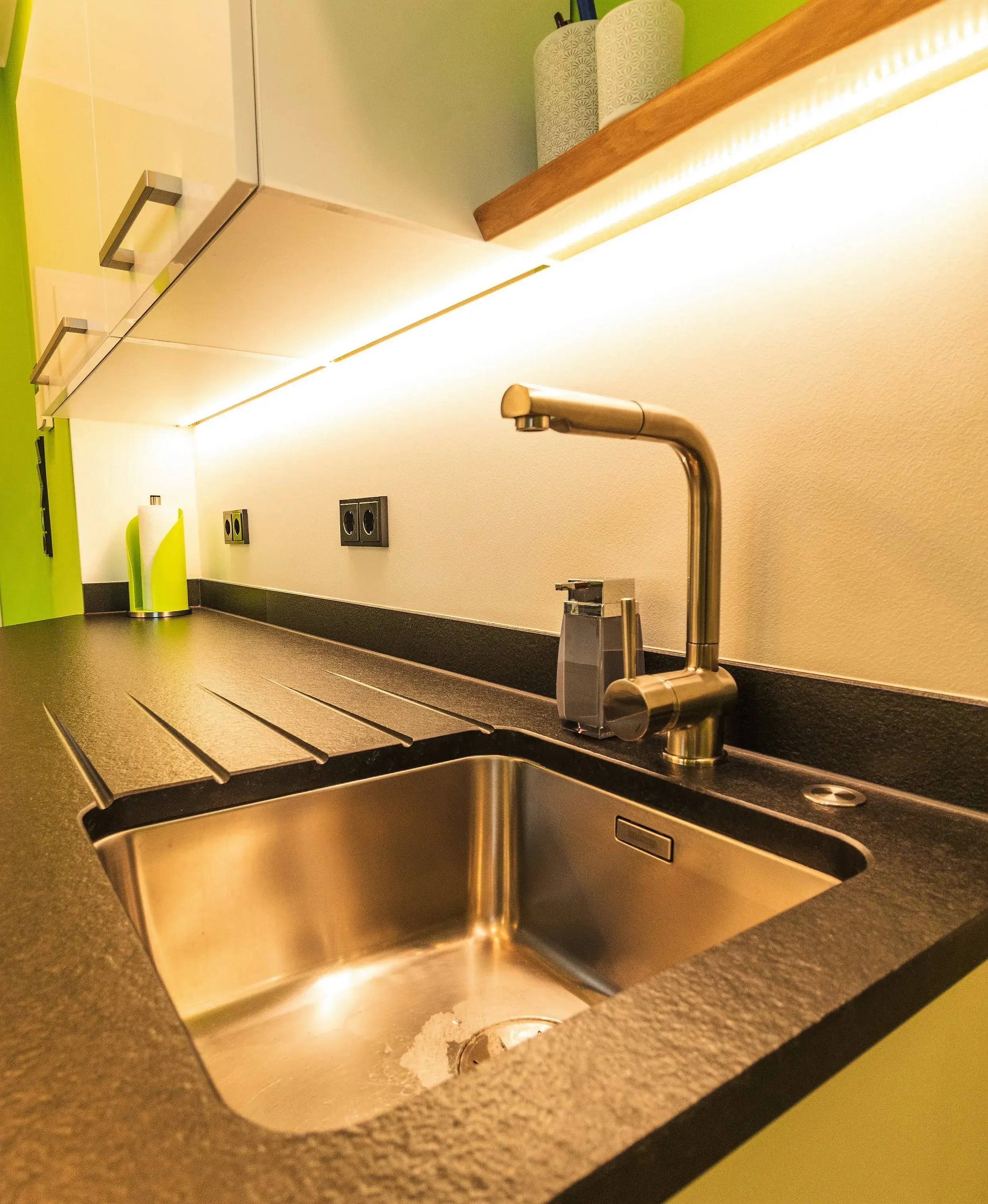 Moderne Küchenspüle mit Wasserhahn und beleuchteter Arbeitsfläche.