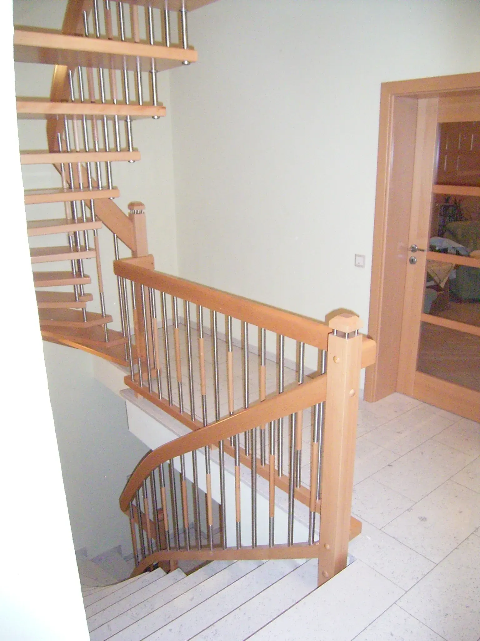 Holztreppe mit Geländer in einem hellen Flur, Tür im Hintergrund.